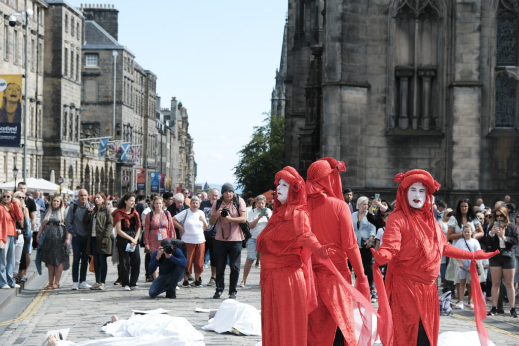 Three XR Die-In participants clothed in red costumes, standing in front of St Giles Cathedral, Edinburgh