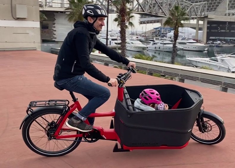 A picture of a man cornering on a Packster cargo bike with a small child riding in the cargo box.